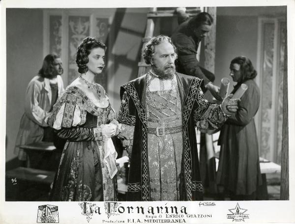 Scena del film "La fornarina" - Guazzoni, Enrico, 1942 - Luigi Pavese guarda a destra e indica con un dito qualcosa che, probabilmente, vede anche Anneliese Uhlig che, con le braccia conserte, osserva.

