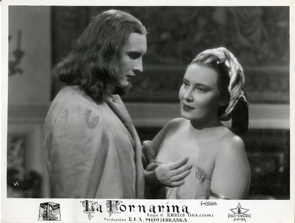 Scena del film "La fornarina" - Guazzoni, Enrico, 1942 - Lida Baarovà, a destra mentre guarda davanti a sé tenendosi il vestito. Di fronte a lei Walter Lazzaro che, di profilo, la fissa.
