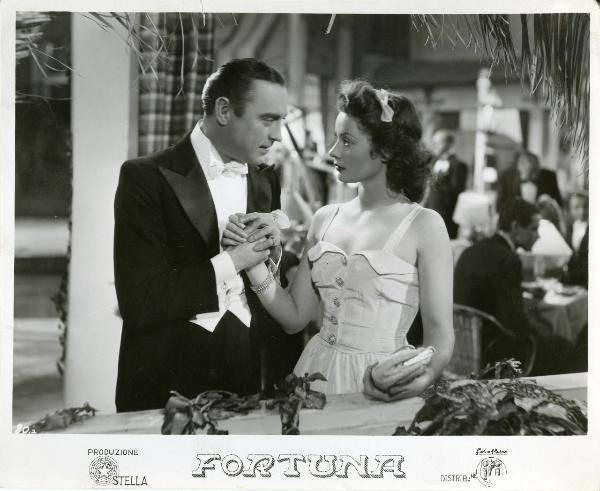 Scena del film "Fortuna" - Neufeld, Max, 1940 - Su un balconcino: Tony D'Algy stringe la mano di Maria Denis guardandola intensamente. Dietro di loro, alcuni attori non identificati.

