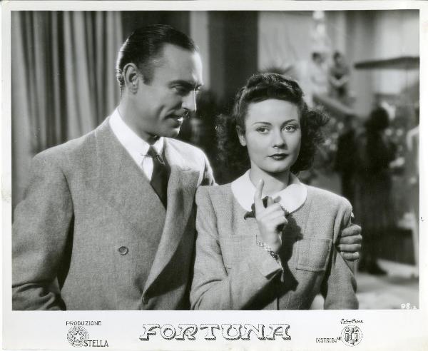 Scena del film "Fortuna" - Neufeld, Max, 1940 - Mezza figura di Tony D'Algy che guarda verso Maria Denis avvolgendola con il braccio sinistro.
