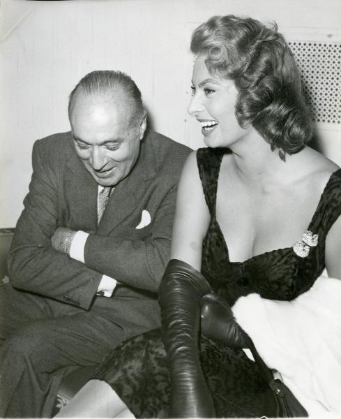 Scena del film "La fortuna di essere donna" - Blasetti, Alessandro, 1956 - Sophia Loren seduta a destra ride e guarda verso sinistra. Accanto a lei seduto un attore non identificato.
