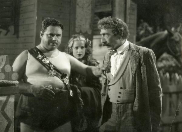 Scena del film "La forza bruta" - Bragaglia, Carlo Ludovico, 1941 - Juan De Landa afferra per la giacca un attore non identificato di fronte a lui. Dietro di loro, Maria Mercader li osserva impaurita.
