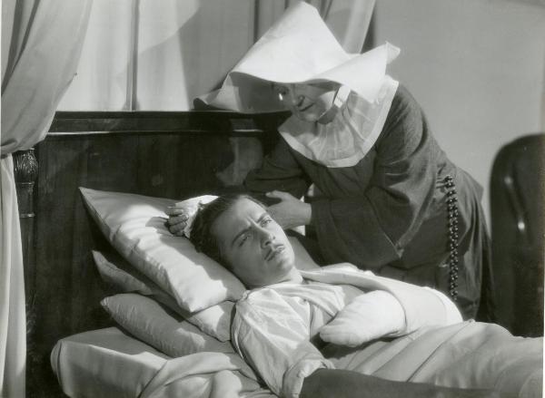 Scena del film "La forza bruta" - Bragaglia, Carlo Ludovico, 1941 - Rossano Brazzi, a letto malato, guarda dritto davanti a sé mentre una suora lo assiste.
