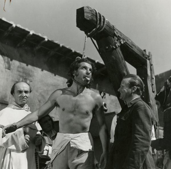 Sul set del film "Fra Diavolo" - Zampa, Luigi, 1942 - Enzo Fiermonte a torso nudo mostra la lingua mentre ha il cappio al collo. A destra, Aldo Quinti, aiuto regista, lo guarda divertito. A sinistra, un attore non identificato in vesti da monaco.