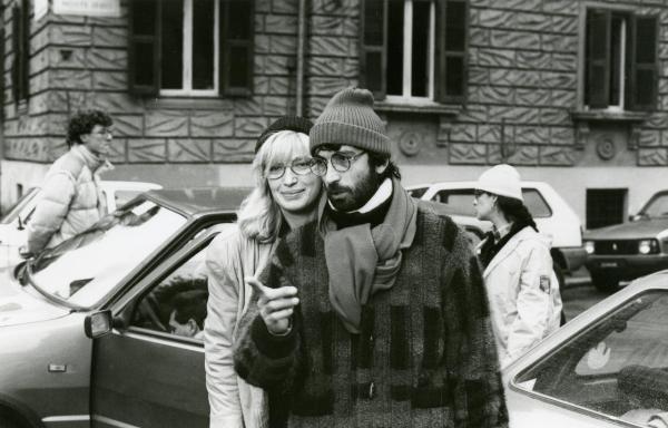 Sul set del film "Francesca è mia" - Russo, Roberto, 1986 - In primo piano, Roberto Russo con alle spalle Monica Vitti. L'attore indica con la mano destra davanti a lui. Dietro di loro, tre attori non identificati intorno a un'auto.
