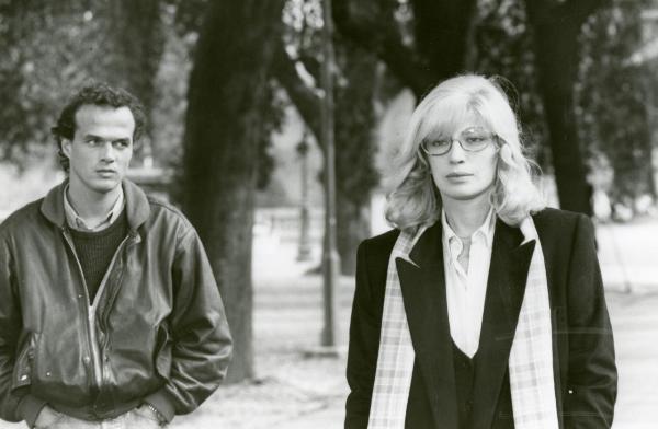 Scena del film "Francesca è mia" - Russo, Roberto, 1986 - Monica vitti, in primo piano a destra, guarda davanti a sé mentre dietro di lei, a sinistra, Pierre Malet la osserva con le mani in tasca.
