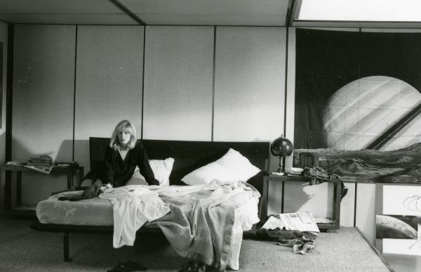 Scena del film "Francesca è mia" - Russo, Roberto, 1986 - In una stanza: Monica Vitti seduta a sinistra del letto disfatto mentre guarda davanti a sé. A destra, un telo raffigurante il pianeta Saturno.
