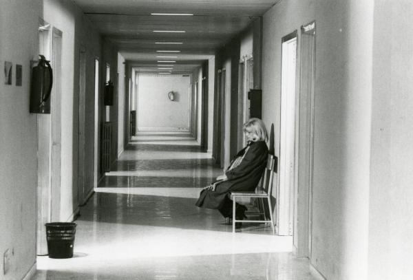 Scena del film "Francesca è mia" - Russo, Roberto, 1986 - Monica Vitti, di profilo seduta sulla sedia nel cOrridoio dell'ospedale, fissa davanti a sé verso il basso.
