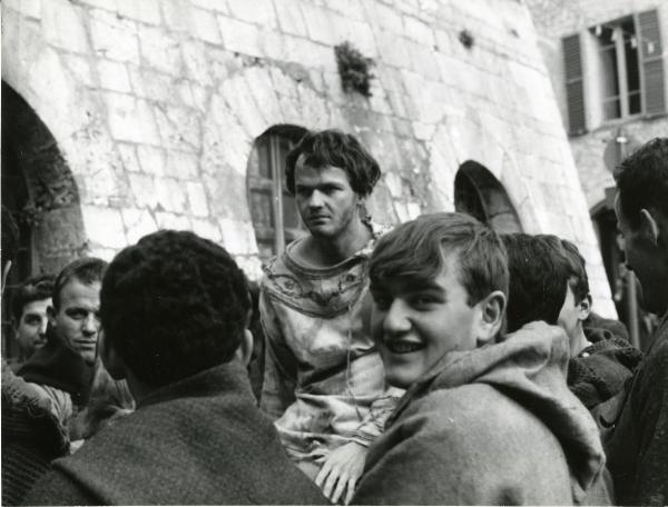 Scena del film "Francesco d'Assisi" - Cavani, Liliana, 1966 - Lou Castel, al centro, in vesti da Francesco d'Assisi, guarda di fronte a sé. In primo piano, un attore non identificato guarda verso la cinepresa. Attorno, attori non identificati.