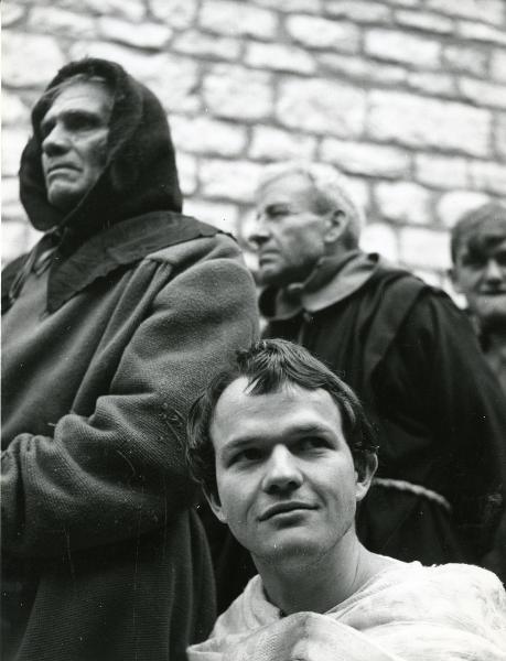 Scena del film "Francesco d'Assisi" - Cavani, Liliana, 1966 - In primo piano in basso, Lou Castel, guarda verso destra. In secondo piano, due attori non identificati hanno lo sguardo rivolto a sinistra.