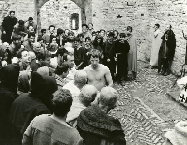 Scena del film "Francesco d'Assisi" - Cavani, Liliana, 1966 - Al centro della scena, Lou Castel a torso nudo ha lo sguardo rivolto verso il basso. Attorno a lui, una folla di frati lo guarda.