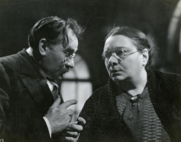 Scena del film "I fratelli Castiglioni" - D'Errico, Corrado, 1939 - Primo piano di Olga Capri a destra mentre guarda dritto davanti a sé e Armando Migliari a sinistra mentre la guarda gesticolando.