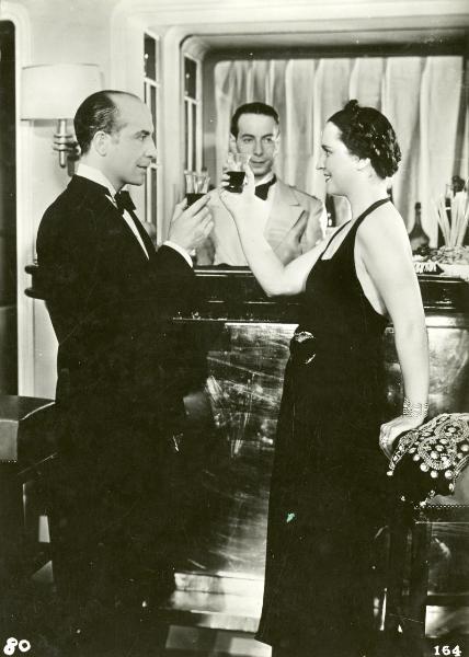 Scena del film "Freccia d'oro" - D'Errico, Corrado, 1935 - In primo piano, un attore non identificato e Vanna Vanni brindano guardandosi negli occhi. Dietro, un attore non identificato nei panni di cameriere li guarda.