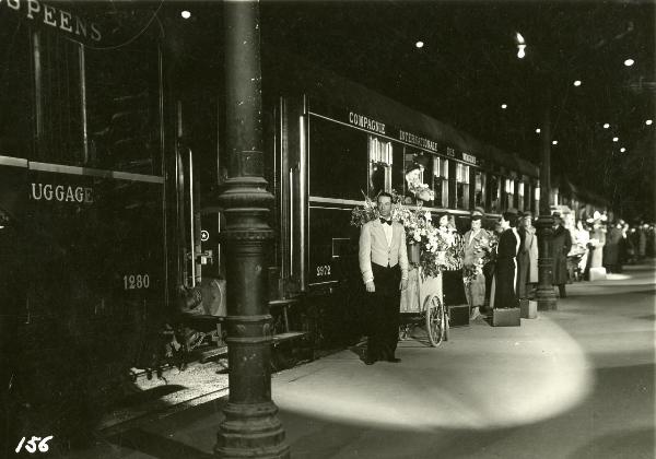 Scena del film "Freccia d'oro" - D'Errico, Corrado, 1935 - Un fila di persone attende di salire sul treno. Al centro, un attore non identificato veste i panni di cameriere di bordo.