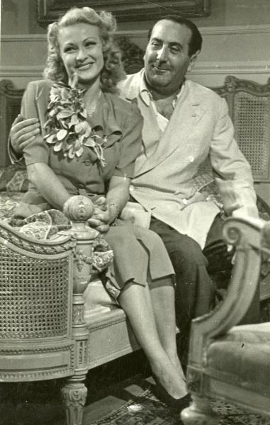 Fotografia sul set di "Frenesia" - Bonnard, Mario, 1939 - A sinistra, Vivi Gioi mentre a destra, il regista Mario Bonnard. Entrambi sorridono con lo sguardo rivolto a sinistra.