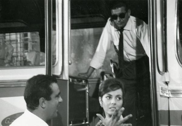 Fotografia sul set di "Frenesia dell'estate" - Zampa, Luigi, 1964 - In primo piano, Marcello Gatti, a sinistra, guarda Michèle Mercier, a destra. Dietro di loro, un attore non identificato all'interno di un pullman si appoggia a due maniglie.