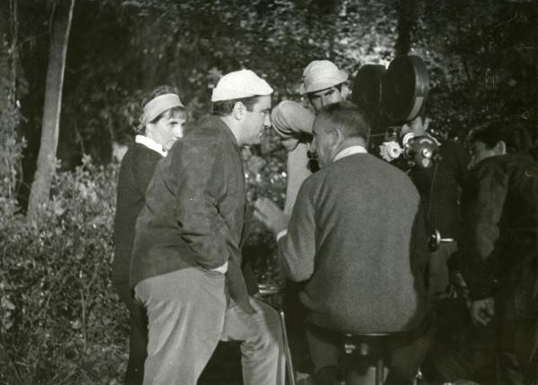 Fotografia sul set di "Frenesia dell'estate" - Zampa, Luigi, 1964 - Il regista Luigi Zampa, di spalle, spiega a Marcello Gatti, a sinistra e con le mani nelle tasche dei pantaloni, la scena. Dietro, alcuni operatori ascoltano le direttive.