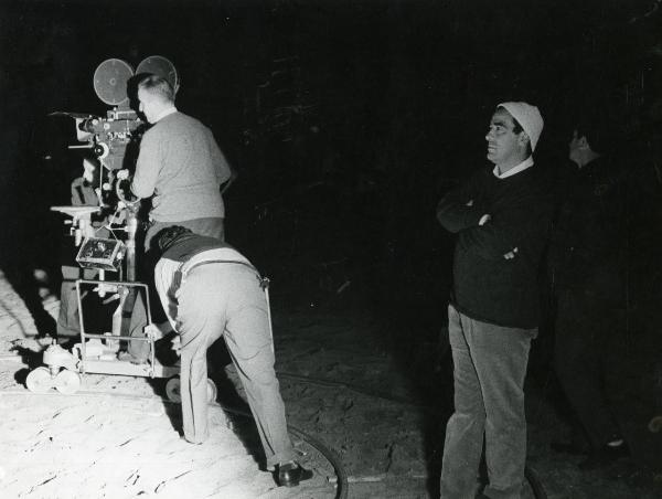 Fotografia sul set di "Frenesia dell'estate" - Zampa, Luigi, 1964 - Illuminati da un faro, il regista Luigi Zampa sposta la cinepresa aiutato da due operatori non identificati. Nella penombra, Marcello Gatti di profilo guarda davanti a sé.