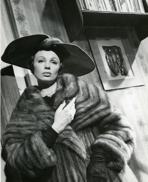 Scena del film "Frou - Frou" - Genina, Augusto, 1955 - Mezza figura di Dany Robin vestita con pelliccia e cappello a tesa larga. L'attrice si porta la mano destra al petto e guarda dritto davanti a sé.