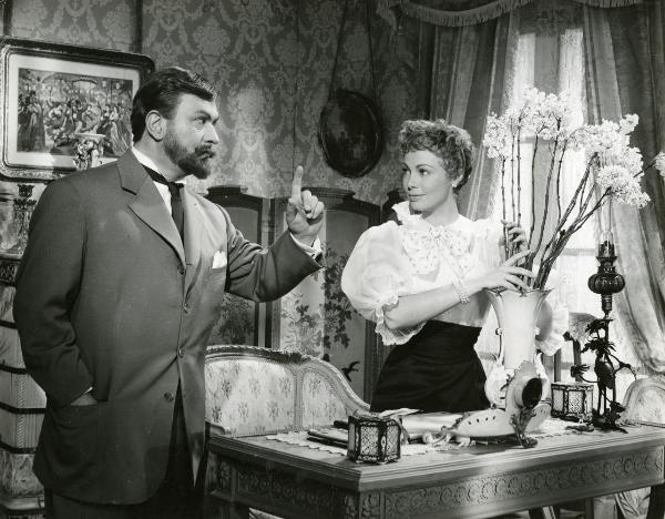 Scena del film "Frou - Frou" - Genina, Augusto, 1955 - In un salotto: a sinistra, Gino Cervi guardando Dany Robin, sulla destra, le punta un dito contro. L'attrice, sorridendogli, sistema un vaso di fiori su una scrivania.