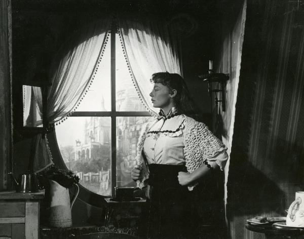 Scena del film "Frou - Frou" - Genina, Augusto, 1955 - Di fronte a una finestra ovale con vista, mezza figura di profilo di Dany Robin con la mano sinistra chiusa a pugno su un fianco.