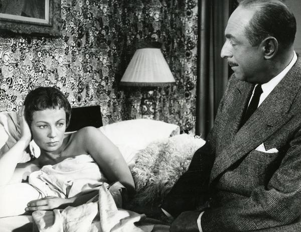 Scena del film "Frou - Frou" - Genina, Augusto, 1955 - Dany Robin sdraiata e nuda sotto le coperte con la testa appoggiata alla mano destra guarda davanti a sé. Di fianco, a destra, un attore non identificato seduto sul letto la osserva.