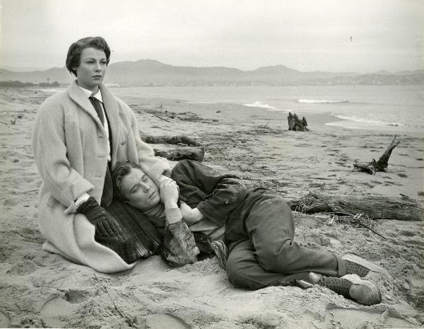 Scena del film "Frou - Frou" - Genina, Augusto, 1955 - Su una spiaggia, a sinistra, Dany Robin è in ginocchio e guarda fisso davanti a sé. Sdraiato sulle gambe dell'attrice, Philippe Lemaire. I due si tengono per una mano.