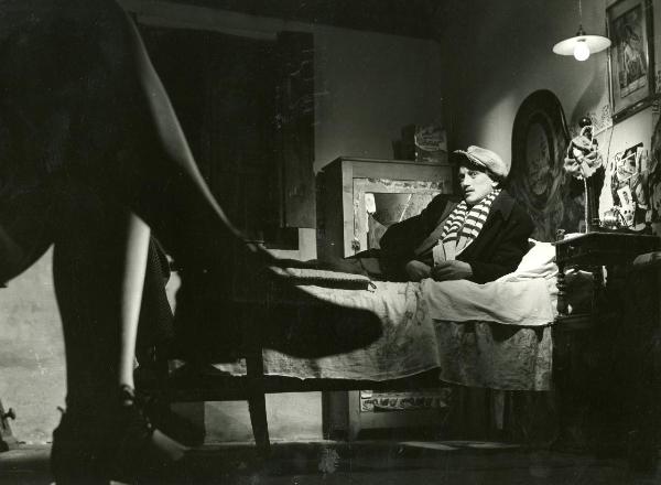 Scena del film "Fuga in Francia" - Soldati, Mario, 1948 - In una camera, Pietro Germi è semisdraiato su un letto e guarda verso la cinepresa. In primo piano, gambe di donna.