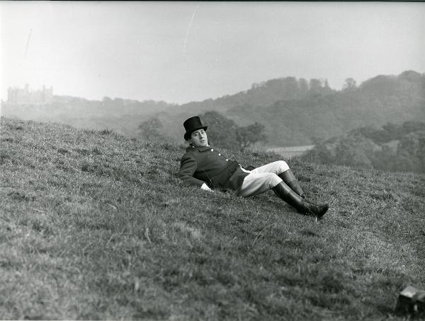 Scena del film "Fumo di Londra" - Sordi, Alberto, 1966 - In mezzo a un campo, Alberto Sordi è semidisteso sui gomiti. Vestito in abiti eleganti, guarda dritto davanti a sé.