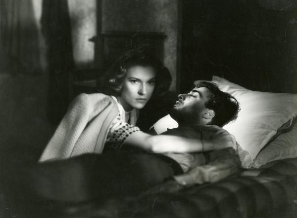 Scena del film "Fumeria d'oppio" - Matarazzo, Raffaello, 1947 - Steso su un letto Armando Francioli dorme. Sopra di lui, mentre guarda dritto di fronte a sé, Mariella Lotti.