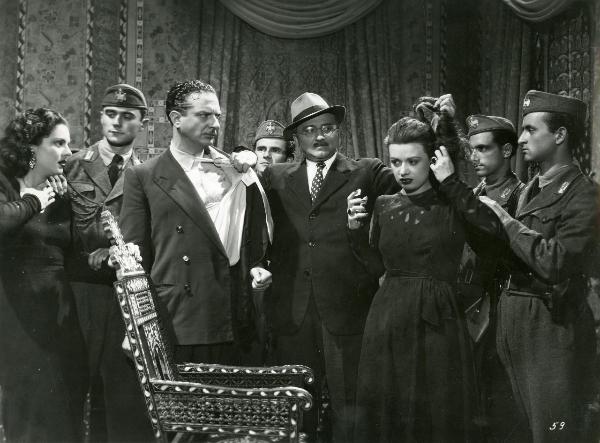 Scena del film "Fumeria d'oppio" - Matarazzo, Raffaello, 1947 - Al centro, Enrico Glori tiene per i capelli un'attrice non identificata mentre con la mano sinistra tiene per il bavaro della camicia un altro attore non identificato.