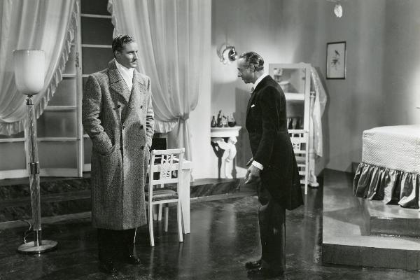 Scena del film "Fuochi d'artificio" - Righelli, Gennaro, 1938 - In una stanza: a sinistra, Amedeo Nazzari vestito con cappotto e sciarpa guarda Giuseppe Porelli, a destra, mentre fa un inchino.