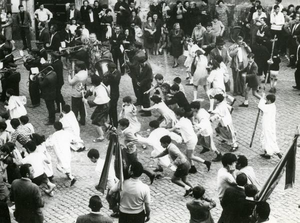 Scena del film "Fuoco" - Baldi, Gian Vittorio, 1969 - In mezzo alla strada, una folla guarda la processione con i musicisti. Al centro, un gruppo di bambini non identificati corre.