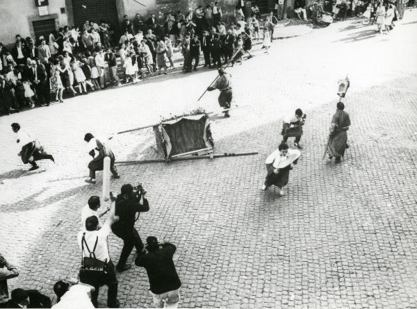 Scena del film "Fuoco" - Baldi, Gian Vittorio, 1969 - Una folla è in procinto di scappare. Al centro, il baldacchino con sopra la statua del santo è ribaltata a terra. A sinistra, alcuni attori non identificati riprendono la scena.