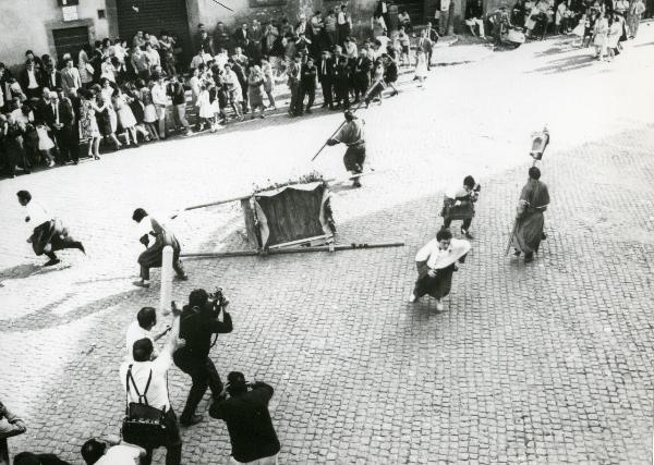 Scena del film "Fuoco" - Baldi, Gian Vittorio, 1969 - Una folla è in procinto di scappare. Al centro, il baldacchino con sopra la statua del santo è ribaltata a terra. A sinistra, alcuni attori non identificati riprendono la scena.