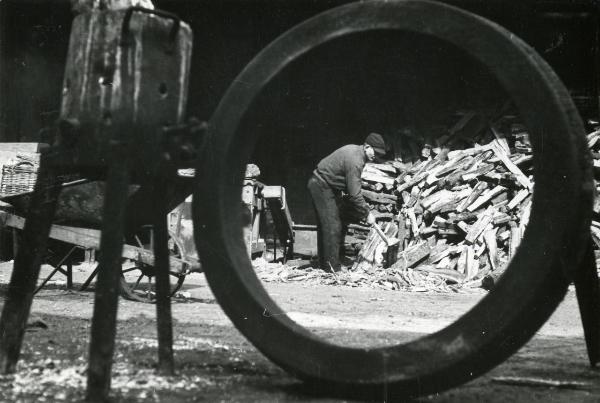 Scena del film "Gamba de legn" - Guerrasio, Guido, 1952 - In primo piano, un oggetto non identificato. Sullo sfondo, un attore non identificato sistema un cumulo di pezzi di legno.