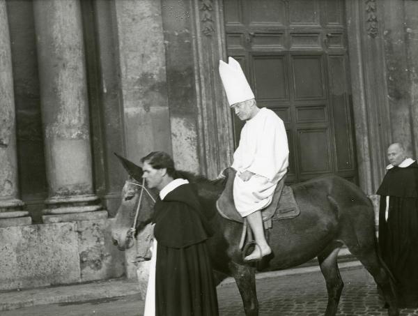 Scena del film "Galileo" - Cavani, Liliana, 1968 - In sella ad un asino, Cyril Cusack guarda dritto di fronte a sé. Un attore non identificato di fianco all'animale, lo trascina. Dietro un altro attore non identificato.