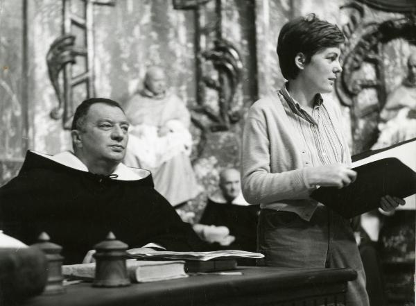 Fotografia sul set di "Galileo" - Cavani, Liliana, 1968 - A destra, la regista Liliana Cavani tiene in mano un quaderno e nel mentre guarda a destra. A sinistra, Gigi Ballista nei panni di commissario dominicano guarda dritto davanti a sé.