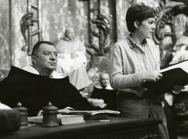 Fotografia sul set di "Galileo" - Cavani, Liliana, 1968 - A destra, la regista Liliana Cavani tiene in mano un quaderno e nel mentre guarda a destra. A sinistra, Gigi Ballista nei panni di commissario dominicano guarda dritto davanti a sé.