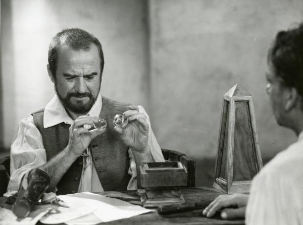 Scena del film "Galileo" - Cavani, Liliana, 1968 - Seduto a una scrivania, Cyril Cusack, a sinistra, sta studiando due oggetti non identificati che tiene tra le mani. A destra, di profilo, un attore non identificato.