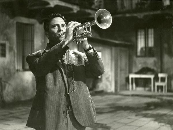 Scena del film "La garconnière" - De Santis, Giuseppe, 1960 - Mezza figura di Raf Vallone mentre suona una tromba e guarda verso sinistra.