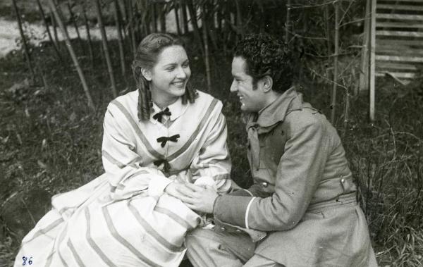 Scena del film "Un garibaldino al convento" - De Sica, Vittorio, 1942 - Seduti in mezzo alle sterpaglie: a destra, Leonardo Cortese e a sinistra, Carla Del Poggio. I due, tenendosi per mano, si sorridono.