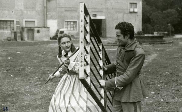 Scena del film "Un garibaldino al convento" - De Sica, Vittorio, 1942 - Divisi da una grata in ferro che tiene tra le mani, Leonardo Cortese e Carla Del Poggio giocano. L'attrice tiene in mano un bastone che punta verso Cortese.