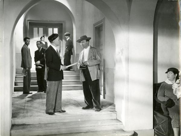 Scena del film "Gatta ci cova" - Righelli, Gennaro, 1937 - Due attori non identificati al centro si guardano. Dietro, quattro attori non identificati. In primo piano a destra, un'attrice non identificata.