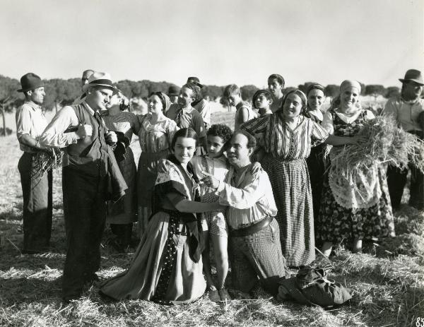 Scena del film "Gatta ci cova" - Righelli, Gennaro, 1937 - In primo piano, da sinistra a destra: una donna, un bambino e un uomo si abbracciano e guardano a sinistra. Dietro, un gruppo di attori non identificati in veste da contadini.