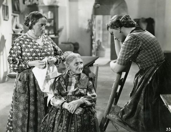 Scena del film "Gatta ci cova" - Righelli, Gennaro, 1937 - A destra, Elli Parvo guarda un'anziana attrice seduta su una sedia al centro. A sinistra, un'altra attrice non identificata tiene in mano una camicia guarda Elli Parvo.