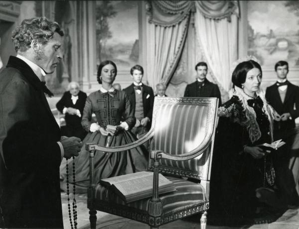 Scena del film "Il gattopardo" - Visconti, Luchino, 1963 - In una sala: in primo piano a sinistra, Burt Lancaster mentre guarda un libro posto su una sedia e regge nelle mani un rosario. A destra, Rina Morelli. Al centro, Lucilla Morlacchi.