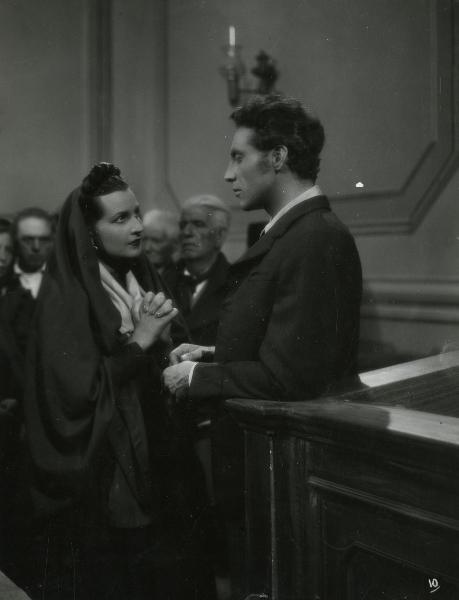 Scena del film "Gelosia" - Poggioli, Ferdinando Maria, 1943 - Roldano Lupi, a destra, appoggiato a un bancone, guarda Luisa Ferida davanti a lui con le mani in segno di supplica.