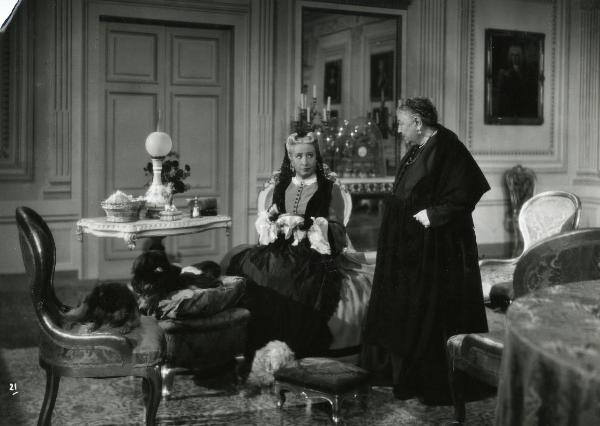Scena del film "Gelosia" - Poggioli, Ferdinando Maria, 1943 -  In un salotto attorno a un tavolino, Wanda Capodaglio seduta ricama e guarda verso Bella Starace Sainati a destra in piedi.