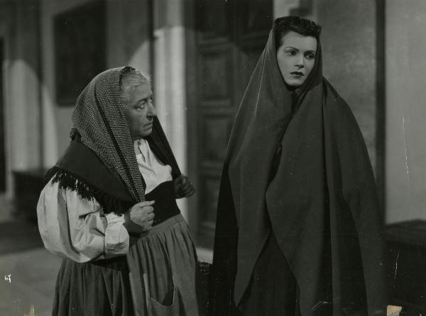 Scena del film "Gelosia" - Poggioli, Ferdinando Maria, 1943 -  A destra, Luisa Ferida, coperta da un velo, guarda a destra. A sinistra, Bella Starace Sainati la osserva tenendosi con le mani i due lembi del velo che porta in testa.